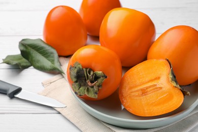 Photo of Delicious ripe juicy persimmons and knife on white wooden table, closeup