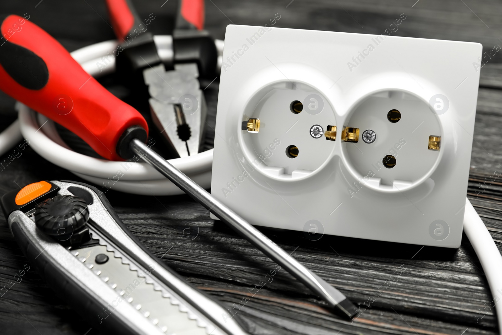 Photo of Set of electrician's tools and power socket on black wooden table, closeup