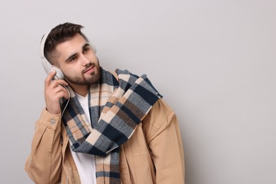 Handsome man in warm scarf listening to music on light grey background. Space for text