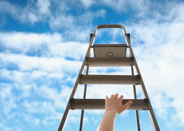 Woman climbing up stepladder against blue sky with clouds, closeup