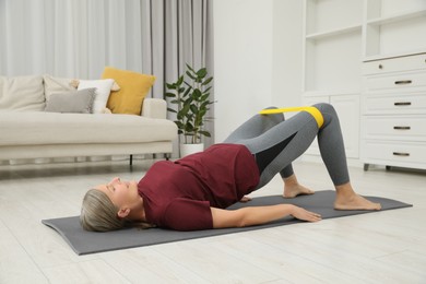 Photo of Senior woman doing exercise with fitness elastic band on mat at home