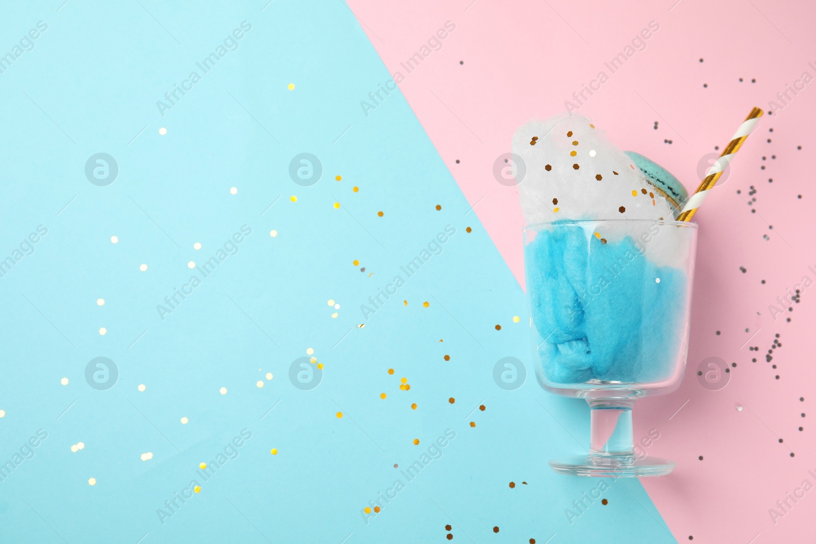 Photo of Glass with cotton candy and macaroon on color background, top view. Space for text