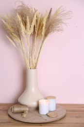 Photo of Vase with decorative dried plants on wooden table near pink wall. Interior design