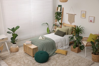 Large comfortable bed and potted houseplants in stylish bedroom. Interior design