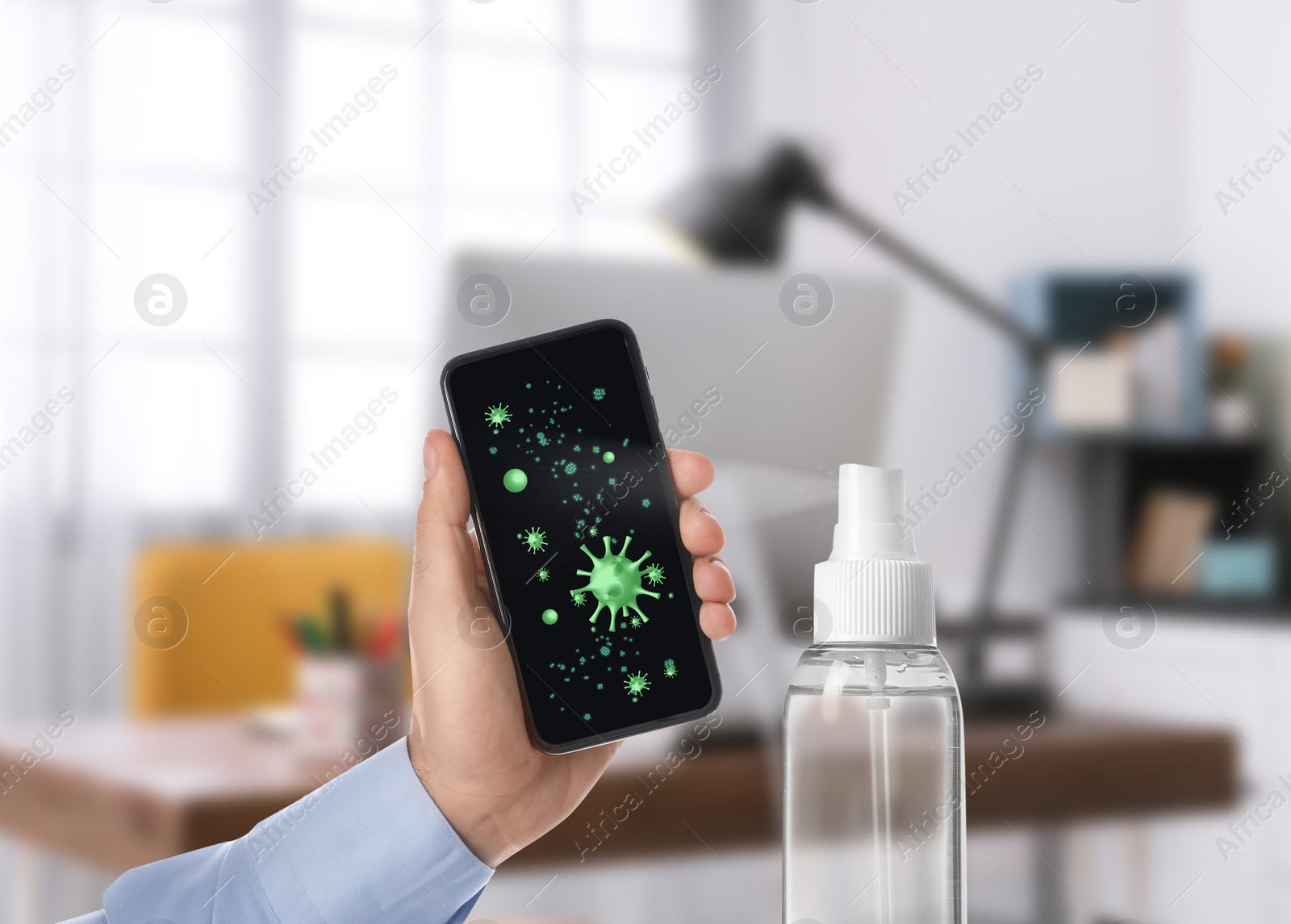Image of Sanitizing mobile devices during coronavirus outbreak. Antiseptic spray and man with smartphone indoors, closeup