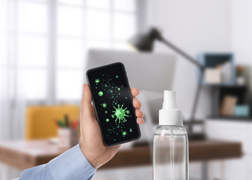 Sanitizing mobile devices during coronavirus outbreak. Antiseptic spray and man with smartphone indoors, closeup