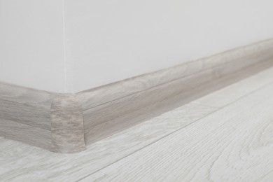 Photo of Wooden plinth with connector on laminated floor near white wall indoors, closeup