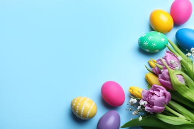 Photo of Bright painted eggs and spring tulips on light blue background, flat lay with space for text. Happy Easter