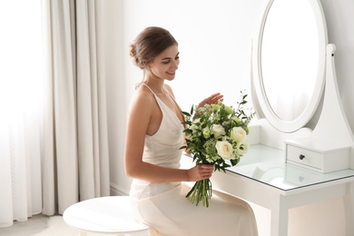 Young bride in wedding dress with beautiful bouquet near mirror indoors