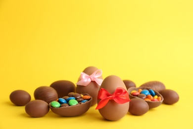 Sweet chocolate eggs with bright candies on yellow background. Space for text