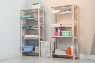 Photo of Wooden shelving units with clean towels and detergents in stylish room interior