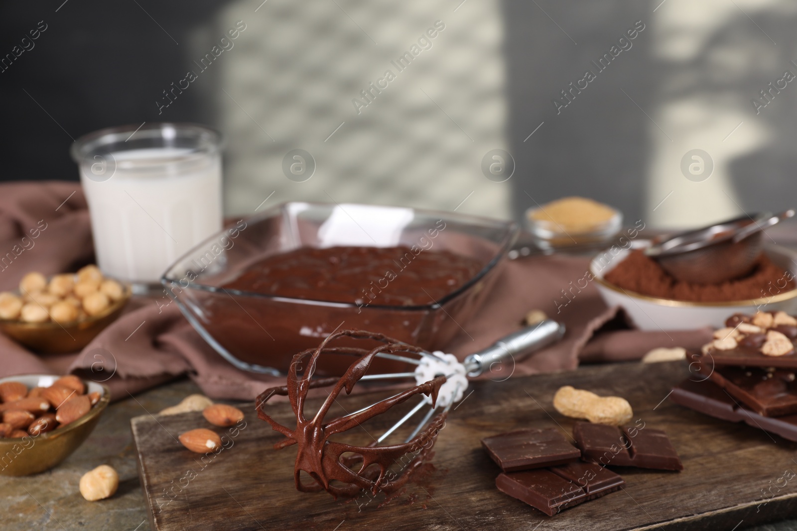 Photo of Whisk with chocolate cream and ingredients on grey table, closeup. Space for text