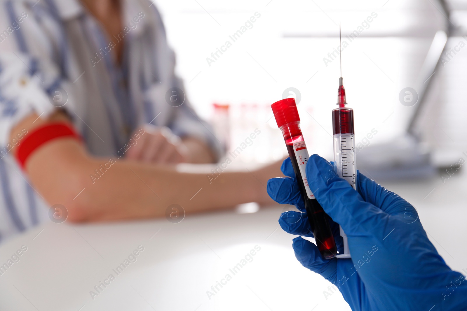 Photo of Nurse holding syringe and sample tube with blood in clinic, closeup. Space for text