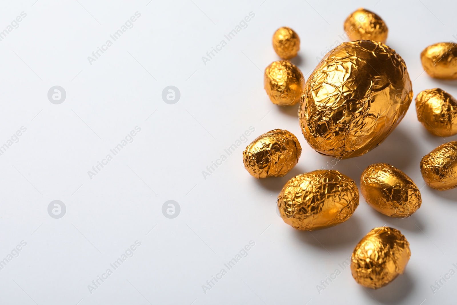 Photo of Chocolate eggs wrapped in golden foil on white background. Space for text