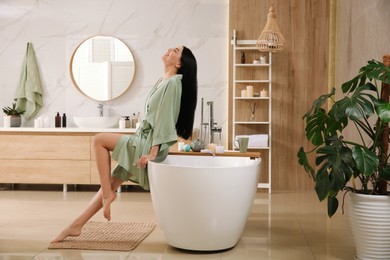 Photo of Beautiful young woman sitting on edge of tub in bathroom