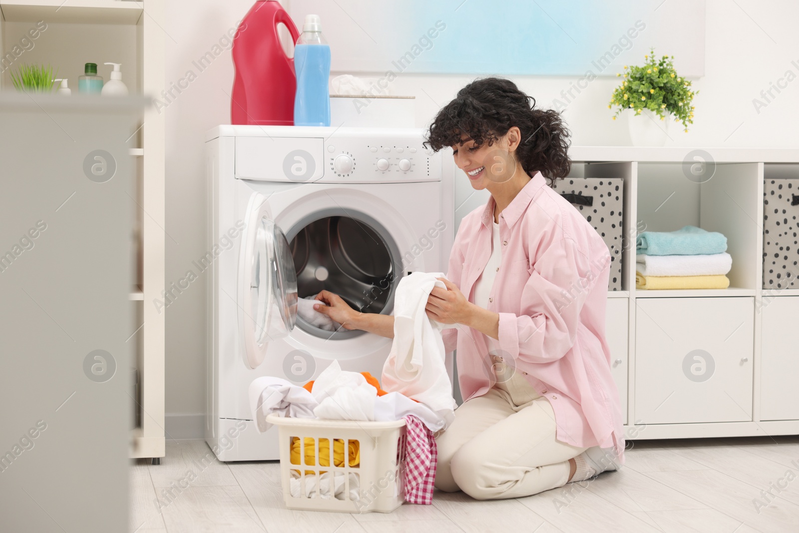 Photo of Happy woman putting laundry into washing machine indoors