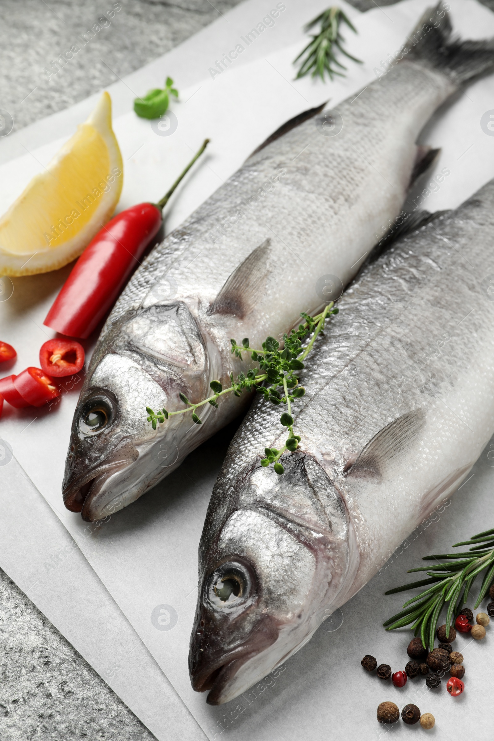 Photo of Sea bass fish and ingredients on grey table, closeup