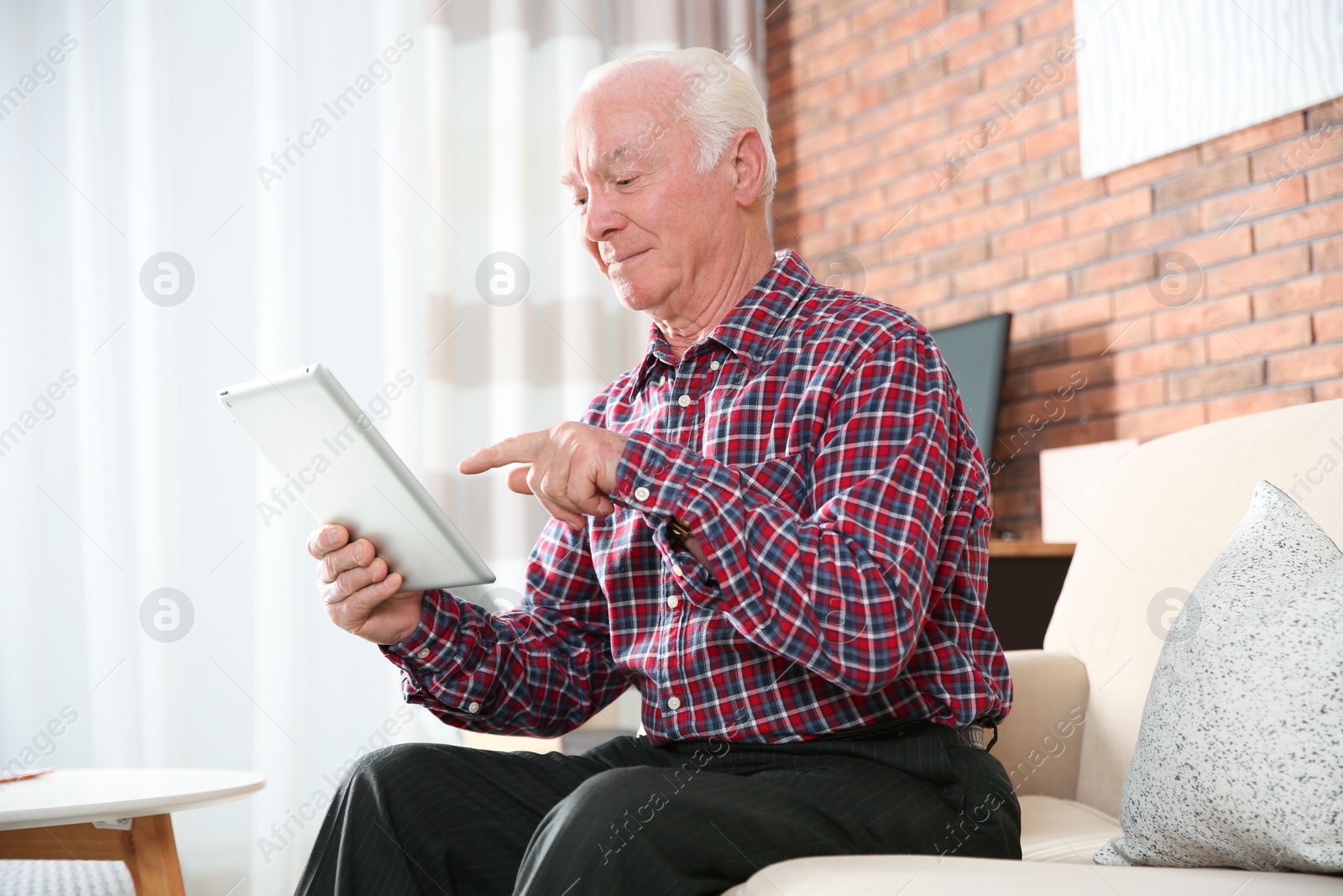 Photo of Elderly man using tablet PC on sofa in living room