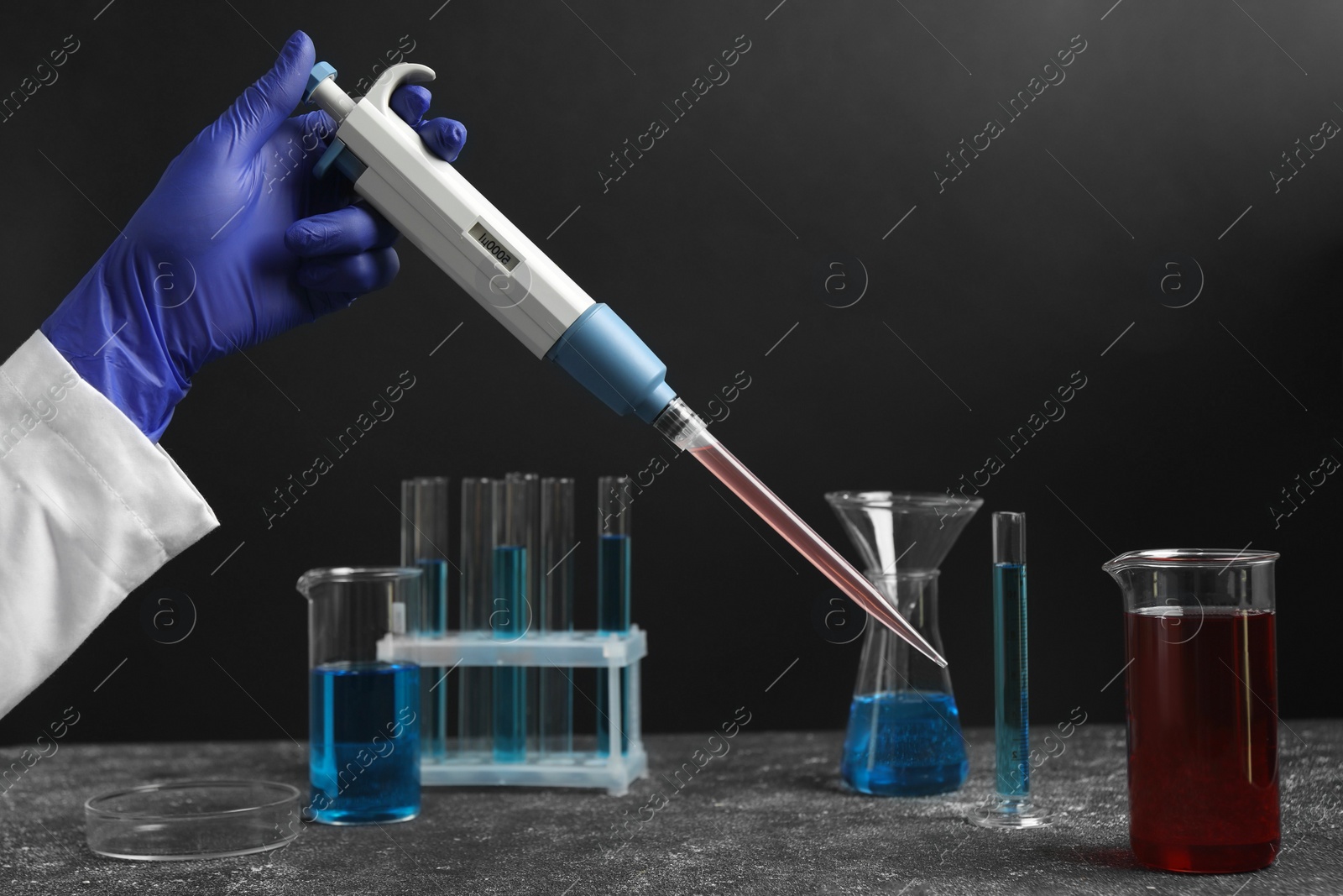 Photo of Laboratory analysis. Scientist holding micropipette with liquid at grey table, closeup