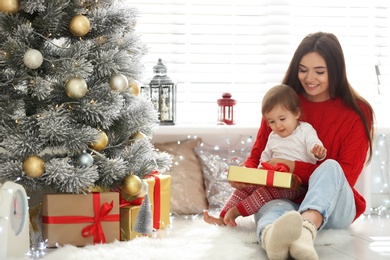 Mother and her cute baby near Christmas tree at home