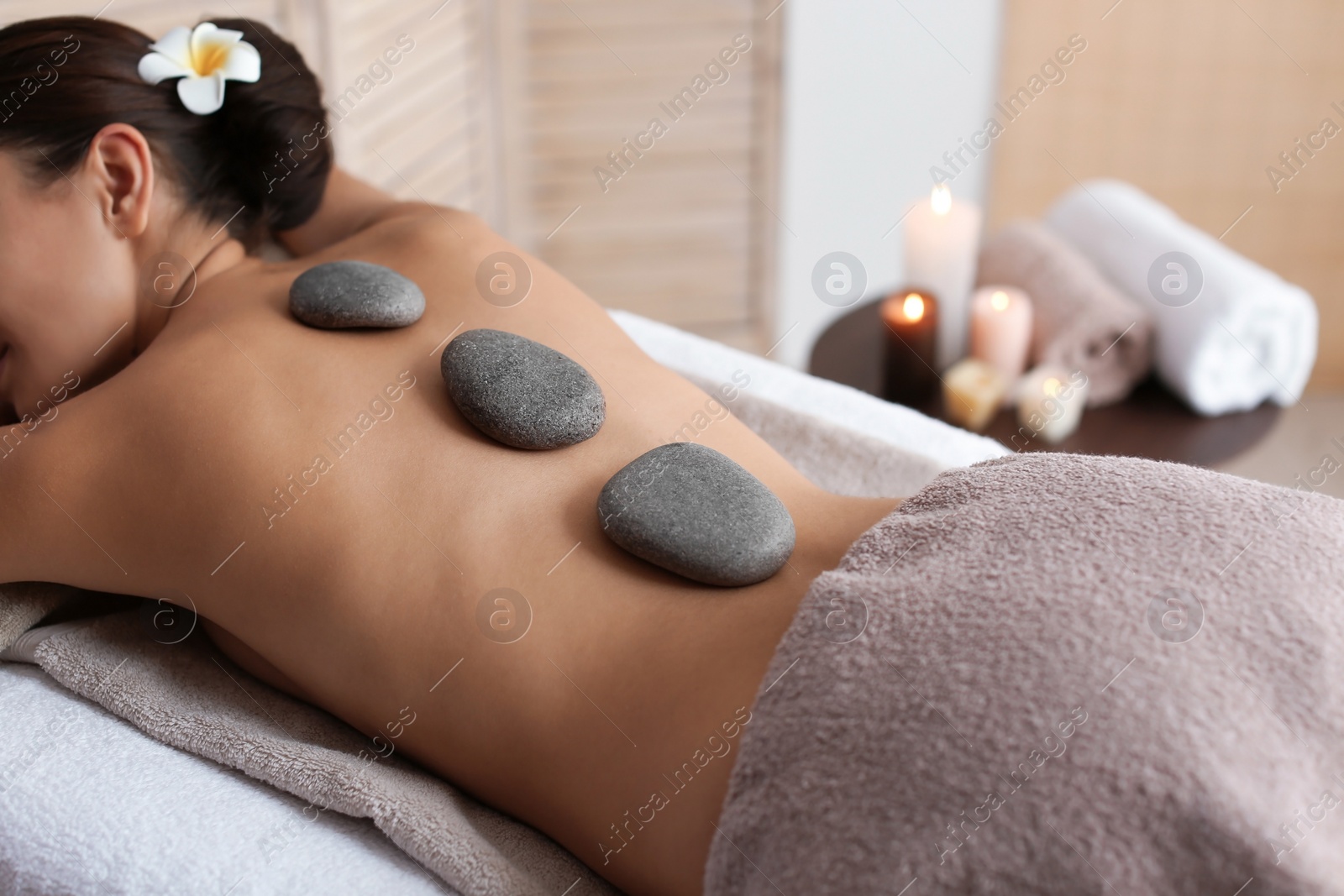 Photo of Beautiful young woman getting hot stone massage in spa salon