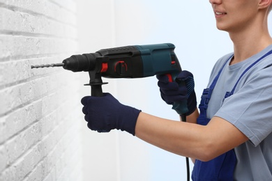 Photo of Young working man using rotary hammer indoors. Home repair