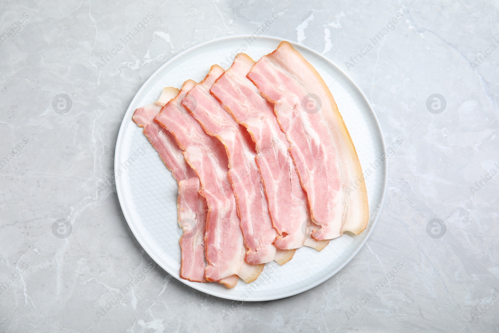 Photo of Plate of sliced raw bacon on light grey marble table, top view