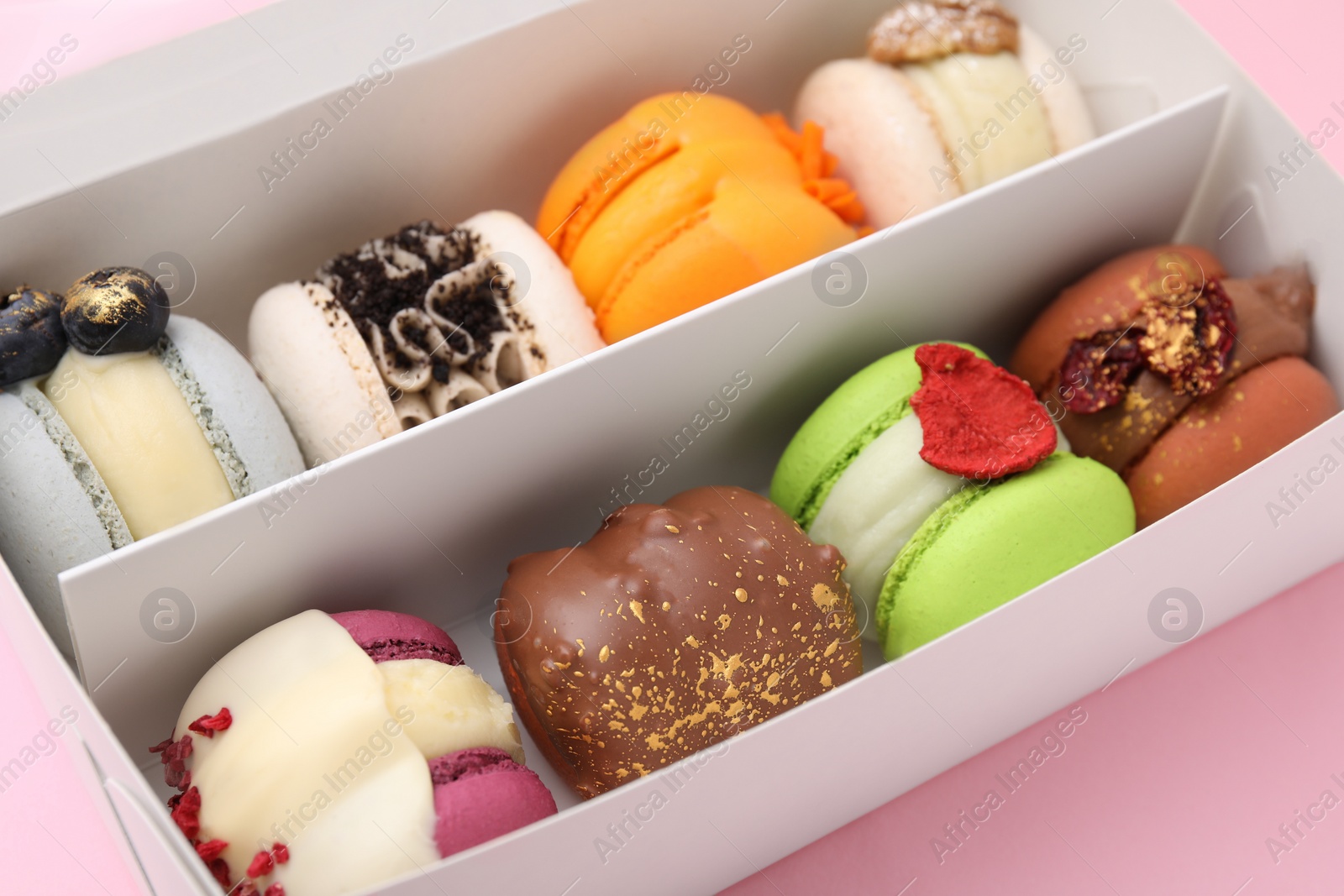 Photo of Cardboard box with delicious macarons on pink table, closeup