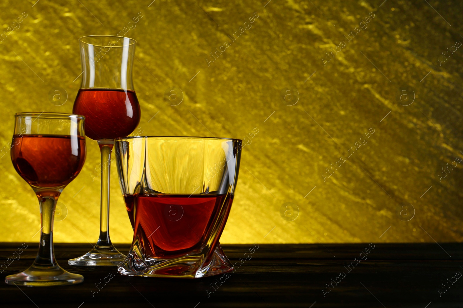 Photo of Different delicious liqueurs in glasses on dark wooden table, space for text