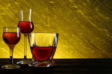 Photo of Different delicious liqueurs in glasses on dark wooden table, space for text