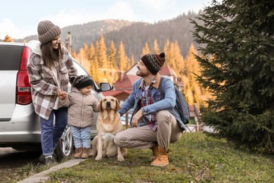 Photo of Parents, their daughter and dog near car in mountains. Family traveling with pet