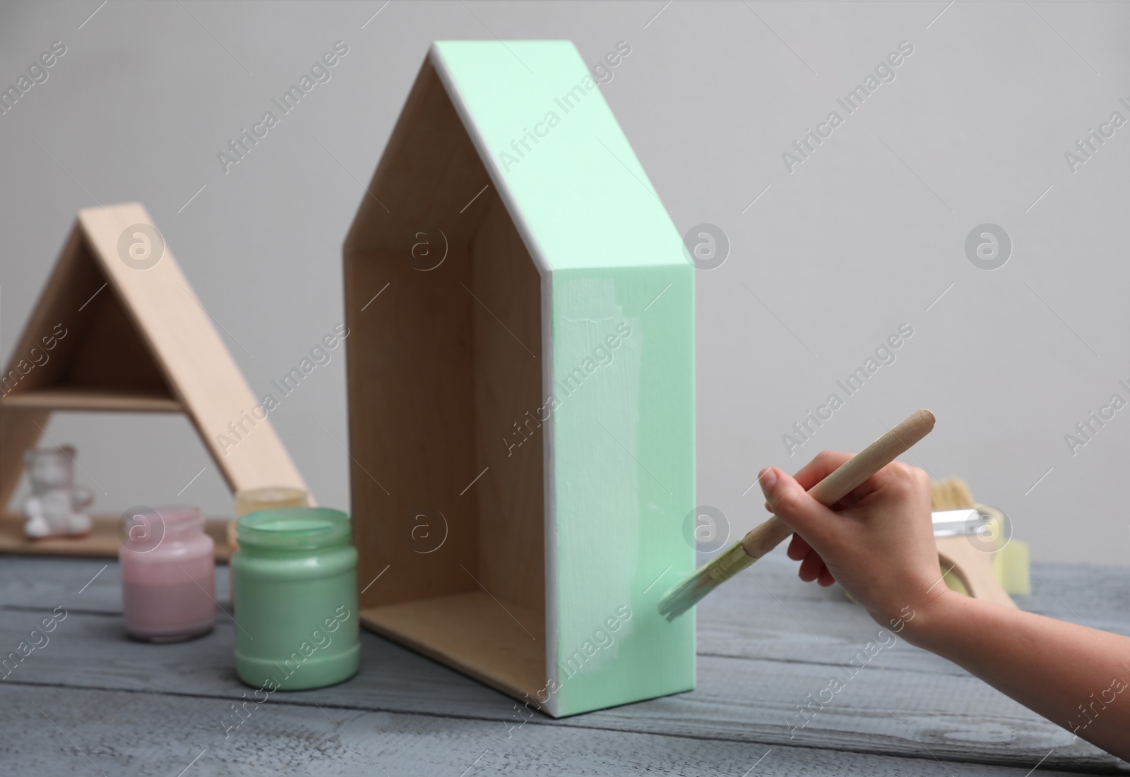 Photo of Woman painting wooden house model at grey table, closeup