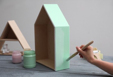 Photo of Woman painting wooden house model at grey table, closeup