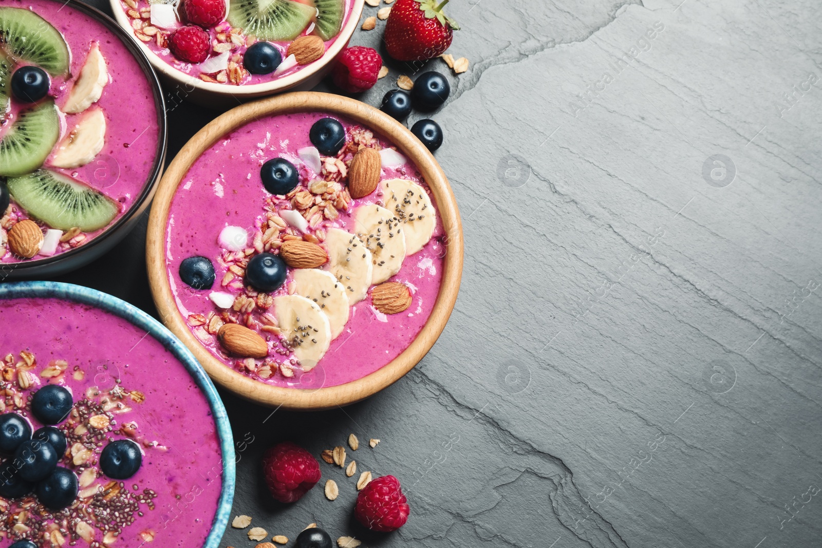 Photo of Acai smoothie bowls with granola and fruits on black table, flat lay. Space for text