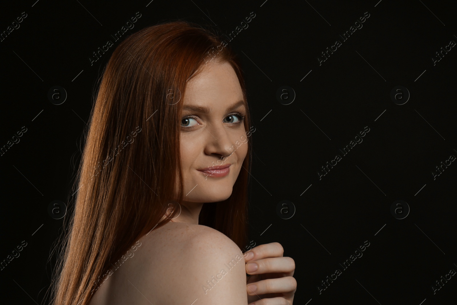Photo of Candid portrait of happy young woman with charming smile and gorgeous red hair on dark background, space for text