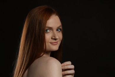 Candid portrait of happy young woman with charming smile and gorgeous red hair on dark background, space for text
