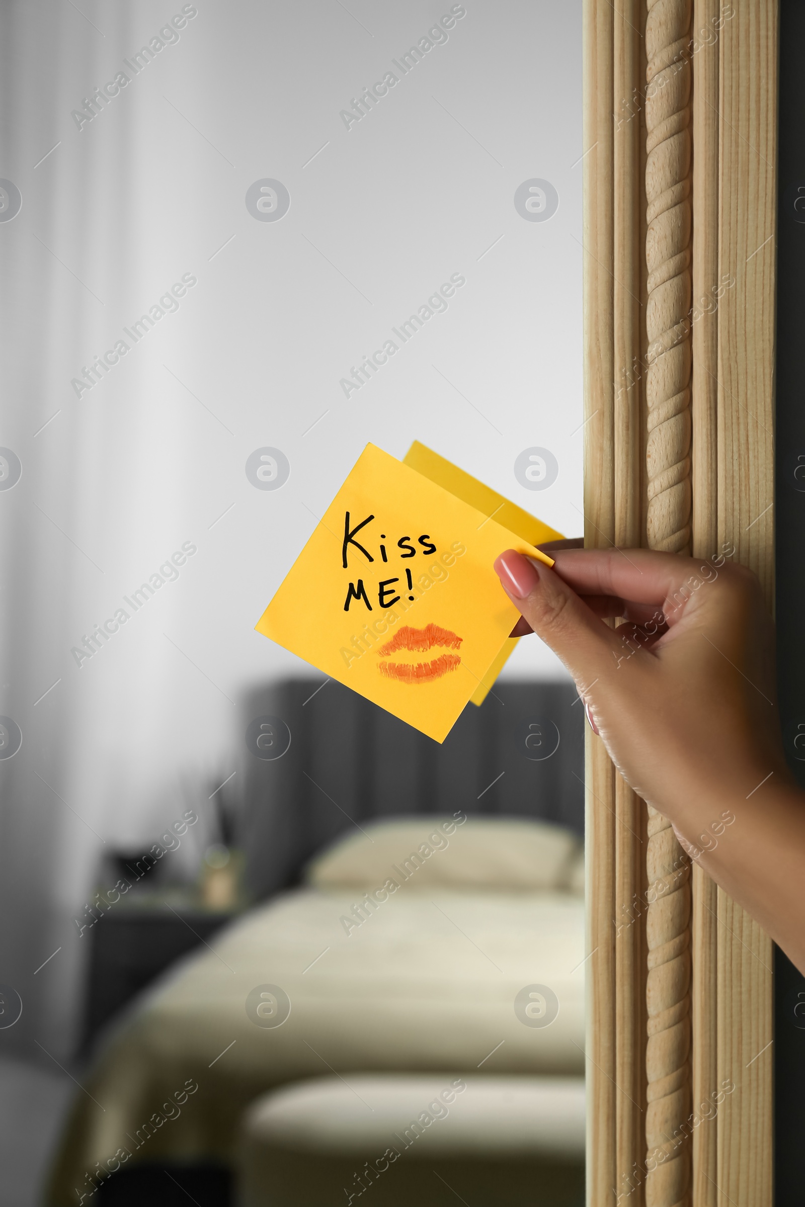 Photo of Woman attaching sticky note with phrase Kiss Me to mirror in room