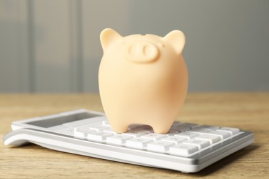 Photo of Ceramic piggy bank and calculator on wooden table