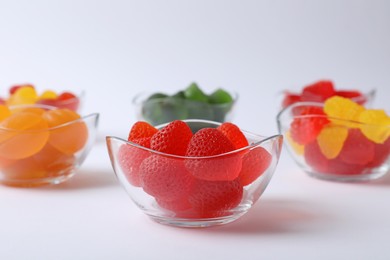 Photo of Different delicious gummy candies in bowls on white background, closeup