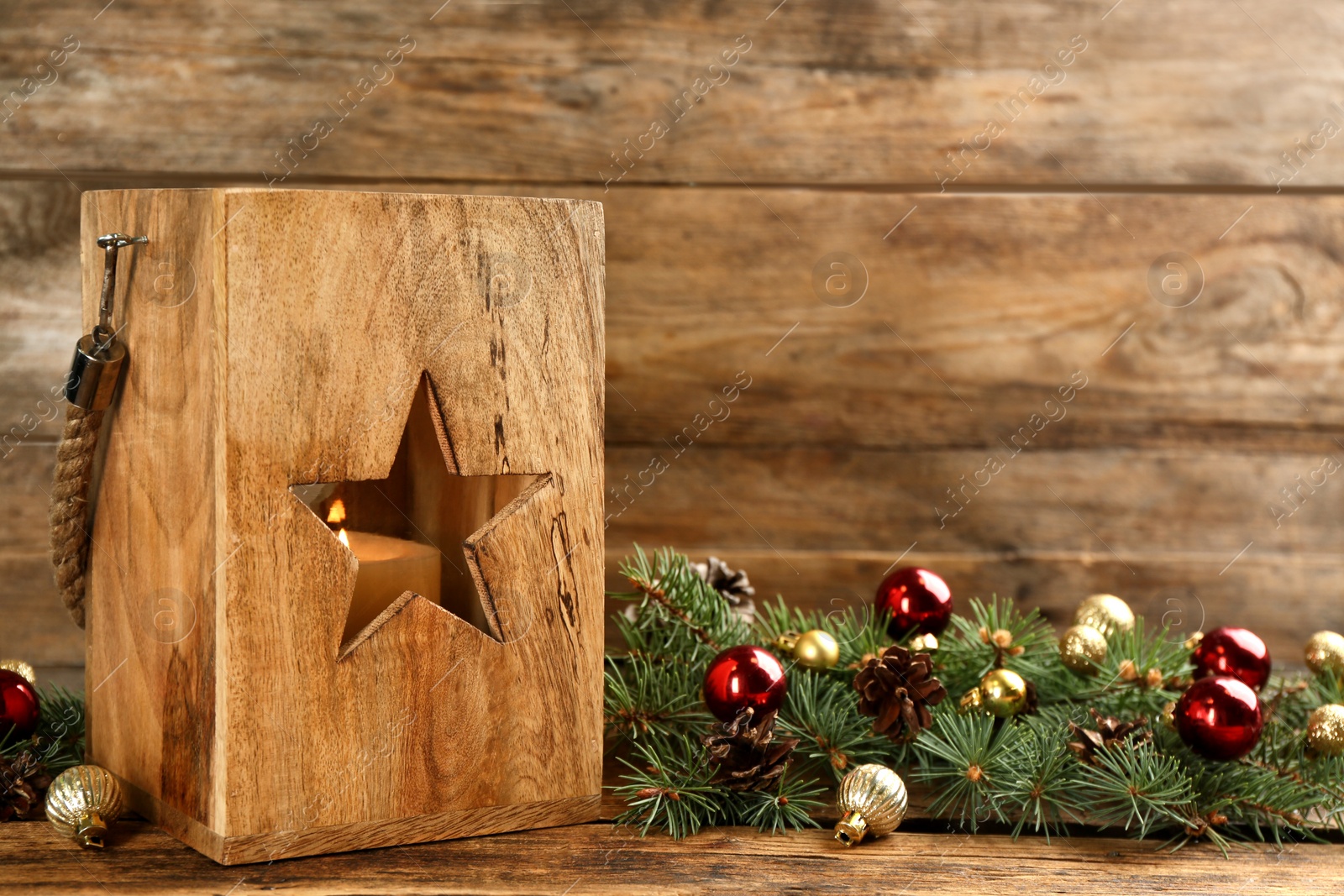 Photo of Christmas lantern with burning candle and festive decor on wooden table. Space for text