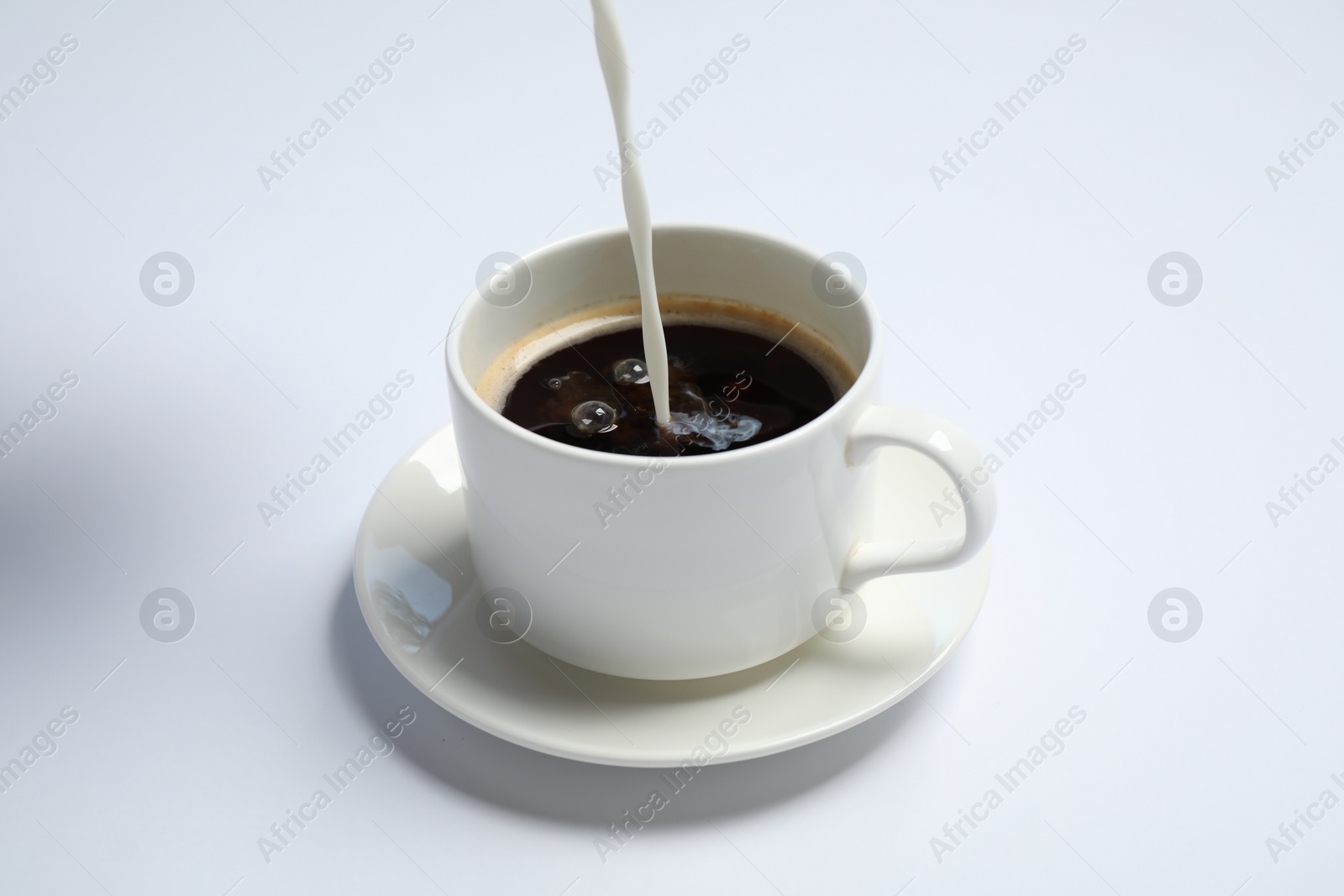Photo of Pouring milk into cup of coffee on white background