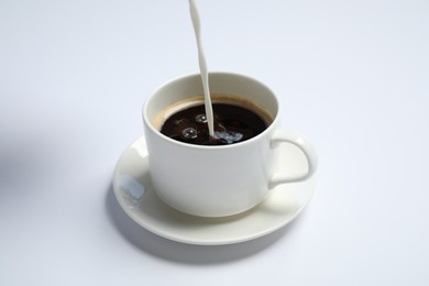 Pouring milk into cup of coffee on white background