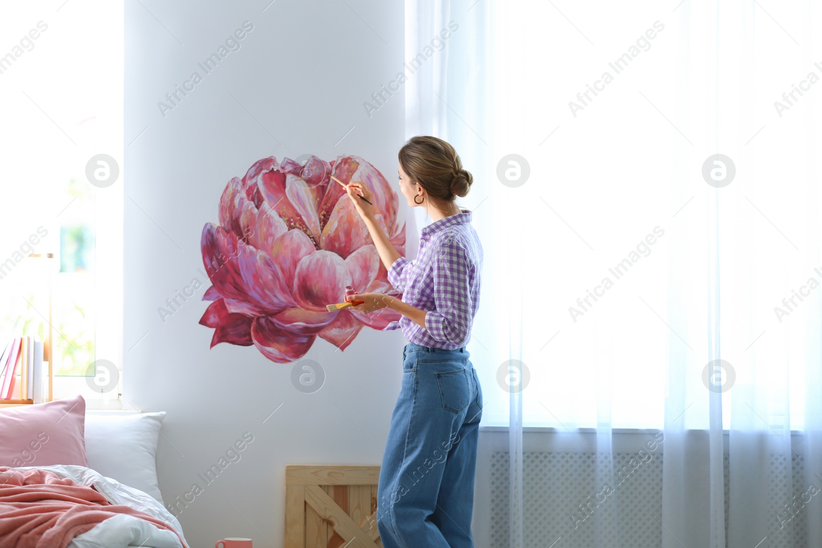 Photo of Young interior designer painting flower on wall in modern room