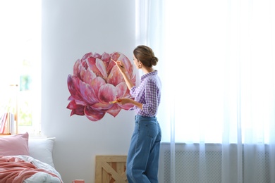 Photo of Young interior designer painting flower on wall in modern room