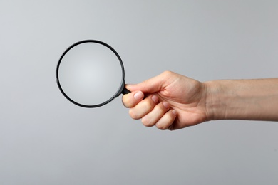 Photo of Woman holding magnifying glass on grey background, closeup. Find keywords concept