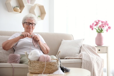Photo of Elderly woman crocheting at home. Creative hobby
