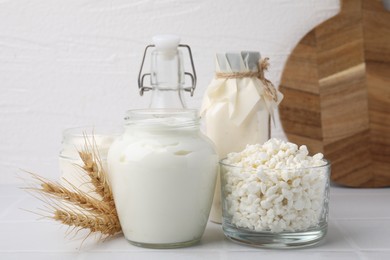 Photo of Different dairy products and spikes on white tiled table