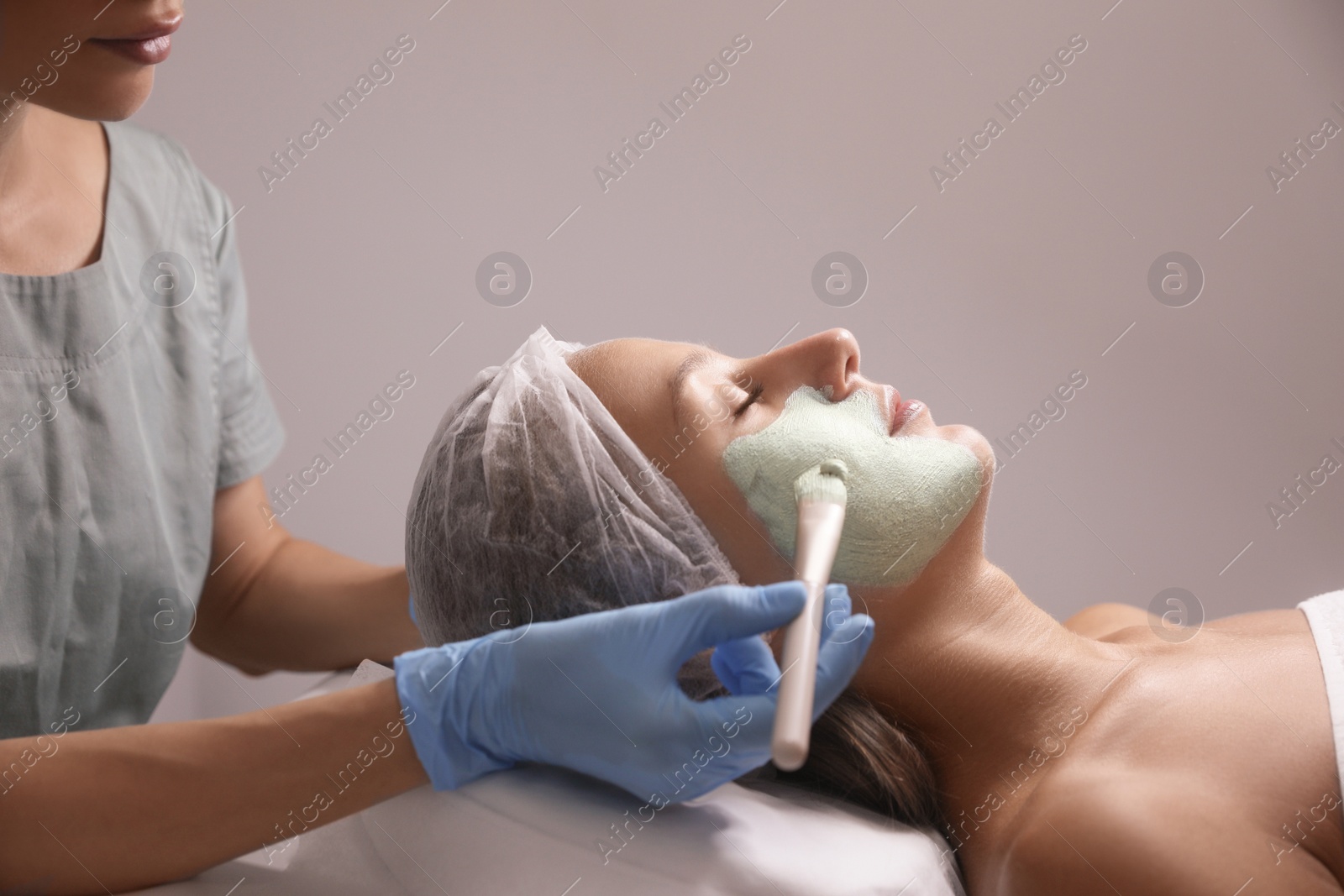 Photo of Cosmetologist applying mask on client's face in spa salon