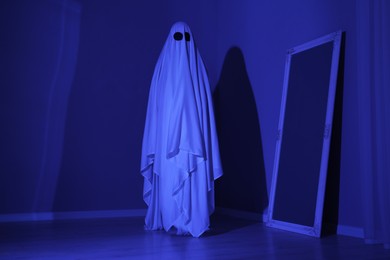 Photo of Creepy ghost. Woman covered with sheet in blue light