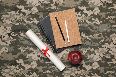 Photo of Diploma, stationery and apple on camouflage background, flat lay. Military education